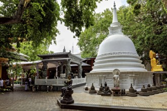 A Buddhist temple complex with a white stupa surrounded by Buddha statues and lush greenery, The