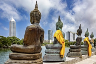 Buddha statues in bronze with yellow cloths in front of skyscrapers and water, The Seema Malaka