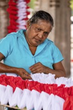 Woman concentrates making red and white decorations, people making garlands in Colombo Sri Lanka