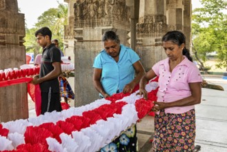 Women making traditional decorations in a temple-like building, people making garlands in Colombo
