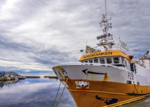 Yellow and white ship in quiet harbor with cloudy sky in the background, Berlevag, Finnmark,
