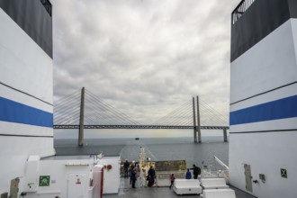 View from a ship of the Øresund bridge under a cloudy sky, wind turbines in the sea under a vast,