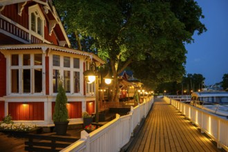 Wooden walkway promenade with red wooden house on an illuminated promenade at dusk, cozy atmosphere