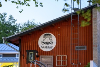 Street scene in the old town of Naantali, wooden cabin with humorous bar sign at dusk, surrounded