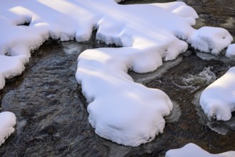 Ilsenburg, Saxony-Anhalt, Germany, Snow-covered ice floes over a flowing stream in winter on the