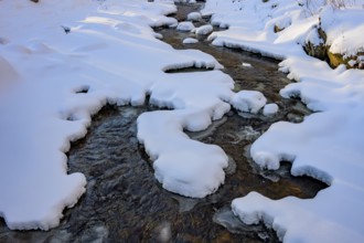 Ilsenburg, Saxony-Anhalt, Germany, A stream flows through a snow-covered landscape with layers of