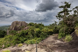 Rocky landscape with cloudy sky and lush green vegetation, a path leads through the scene, The