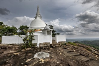 White stupa on rocky hill surrounded by cloudy skies and lush nature, The Maligatenna Purana