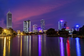 Nighttime city view with brightly lit skyscrapers and colorful sky mirror in the water, the skyline
