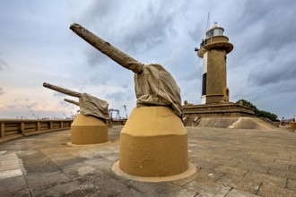 A lighthouse next to two cannons on a paved area under a cloudy sky, The Colombo Sri Lanka