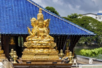 Golden Buddhist statue in front of a blue roof with cloudy sky, The Seema Malaka Temple with the