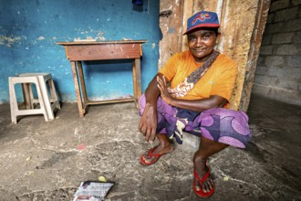 Smiling man wearing cap squats relaxed in a simple room, people in the streets of Slave Island in