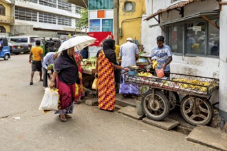 People shop at market stalls in a lively street scene, people on the streets of Slave Island in