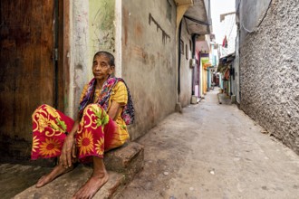 Elderly woman sitting pensively in a narrow alley, people in the streets of Slave Island in Colombo