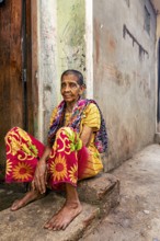 Woman in colorful clothes sitting on a step in a narrow street, people in the streets of Slave