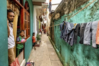 Children look out of a window, laundry hangs in a narrow alley, people in the streets of Slave