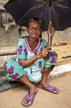 A woman sits relaxed under an umbrella in colorful clothes and smiles serenely, praying people at