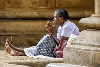 A woman sits in front of a stone temple and prays, surrounded by peace and traditional atmosphere,