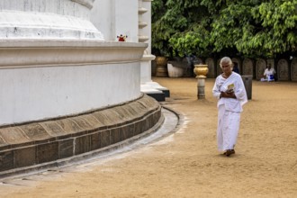 A man in meditative posture walks around a large white temple with a book, People praying at