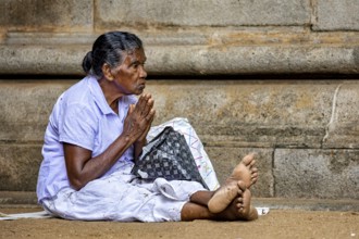 Elderly woman in humble position praying in front of a stone temple, with peaceful expression,
