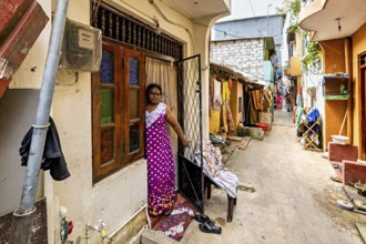 Woman in traditional dress standing in front of a house in the alley, people in the streets of
