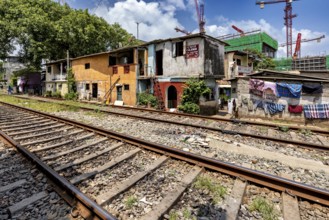Construction cranes rise behind brightly painted houses along the train tracks under a blue sky,