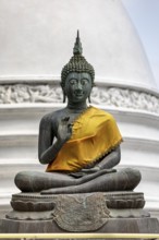 Bronze Buddha statue with yellow cloth in front of a white temple, The Seema Malaka Temple with the