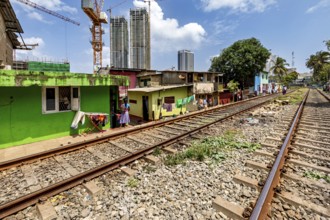 Railway tracks next to colorful houses with skyscrapers in the background and construction crane