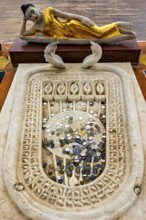 A reclining Buddha statue with gold robes above a carved stone surface filled with coins,