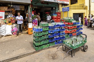 A small shop with boxes full of bottles in front of the entrance, surrounded by busy street