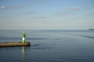 A green lighthouse harbour fire stands on a pier at the port exit of Travemünde in front of a calm,