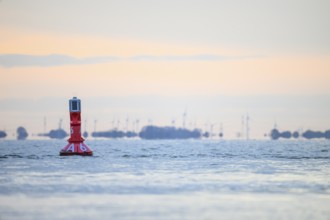 A buoy in the calm sea at sunset with distant wind turbines, Jade Bay, Lower Saxony, Germany
