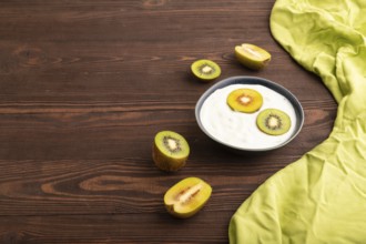 Yogurt, with kiwi in blue bowl on brown wooden background and green linen textile, side view, copy