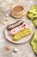 Glazed Eclairs on brown concrete background and green linen textile, cup of coffee, side view,