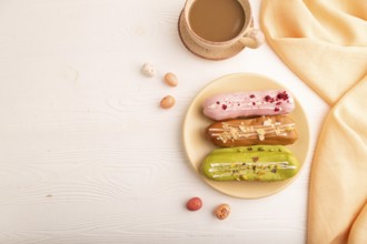 Glazed Eclairs on white wooden background and orange linen textile, cup of coffee, top view, flat