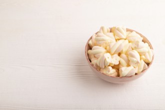 Orange and pink marshmallow in ceramic bowl on white wooden background, side view, copy space,