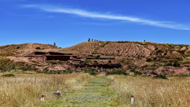 Grassy trail leads to ancient ruins framed by natural landscape under blue skies, the