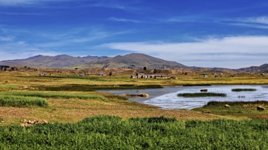 Wide landscape with a lake surrounded by meadows and small villages under a blue sky, The landscape