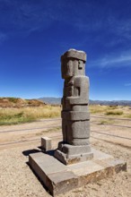 Ancient stone figure standing upright on a platform against a clear sky, the archaeological site