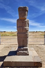 Ancient stone statue on a base in an open-air area under clear skies, The archaeological site with