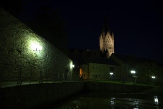 A Gothic church illuminated at night with illuminated tower and dark sky in the foreground the