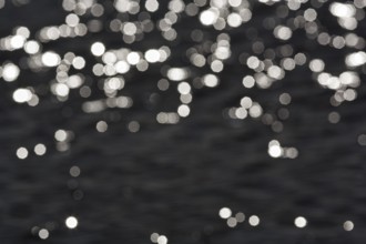 Abstract black background, sparkling white lights, bokeh balls, light reflections on water surface,