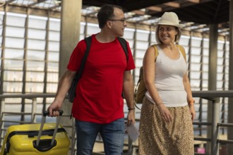 Adult travel couple walking together inside a modern airport terminal, carrying luggage and travel