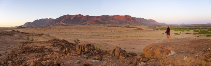 Young woman standing in desert landscape with Brandberg in morning light, at sunrise, Erongo,