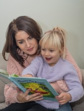 A mother reads a book together with her blonde girl, 4 years old, in Ystad, Skåne County, Sweden,