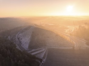 Landscaped hills in the pink-yellow light of sunrise, old deposit, construction site for PV open