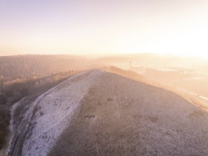 A snow-covered hill with sunrise and fog in the background, old deposit, construction site for PV