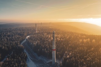 Sun rays over a foggy forest and wind turbine towers rising from the tree cover, Windkraft Bau,