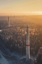 Wind turbine towers over snow-covered trees, the warm light and the fog create a mystical scene