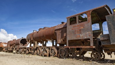 Long line of rusty locomotives in an open desert landscape under clear skies, old rusty locomotives